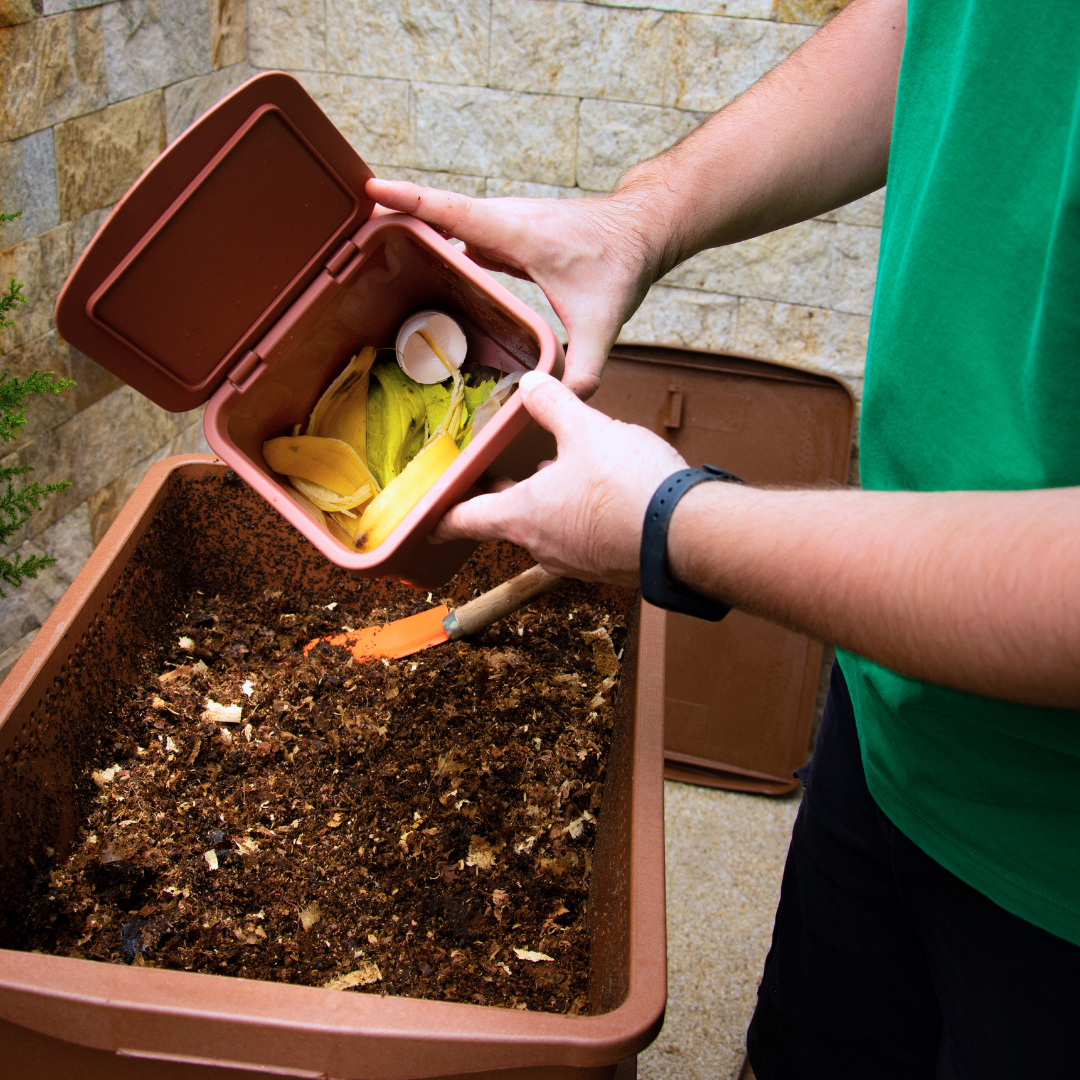 Person dumping a box of compost into a tub of soil.
