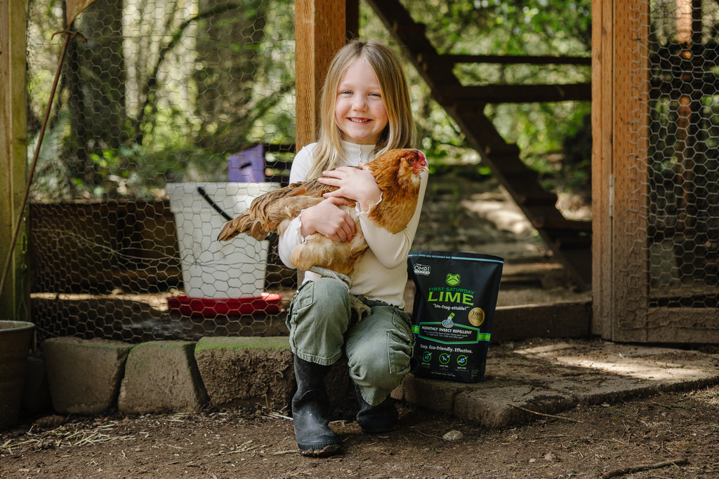 A young girl outside of a chicken coop, smiling and holding a chicken.