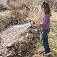 Child watering plants with a First Saturday Lime hose in a garden setting