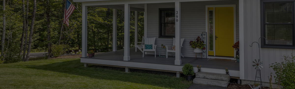 Front porch of a house with a yellow door and American flag, surrounded by greenery.