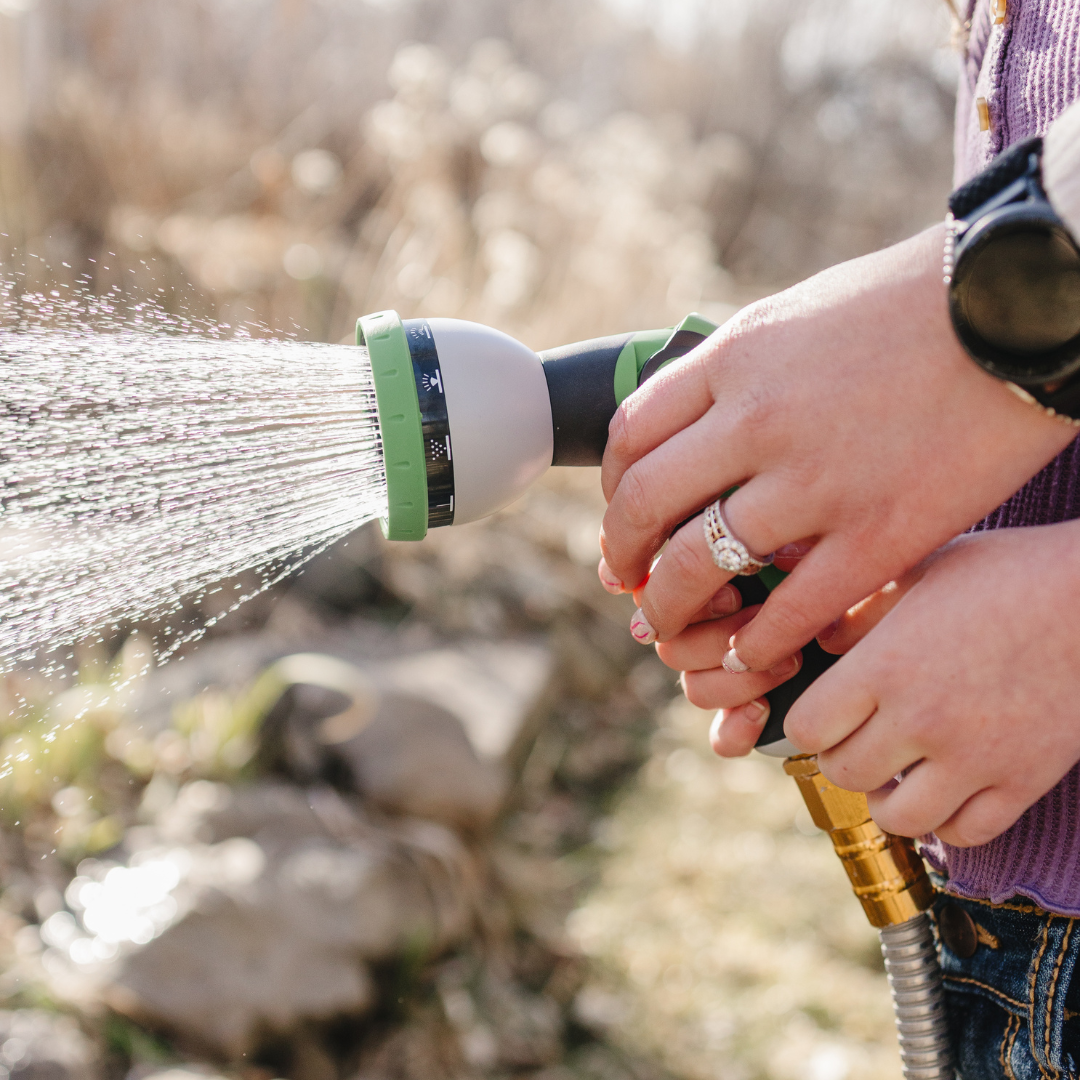 Person holding a garden hose spraying water outdoors.