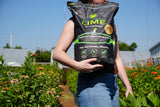 A woman holds a bag of First Saturday Lime in a large garden of flowers.