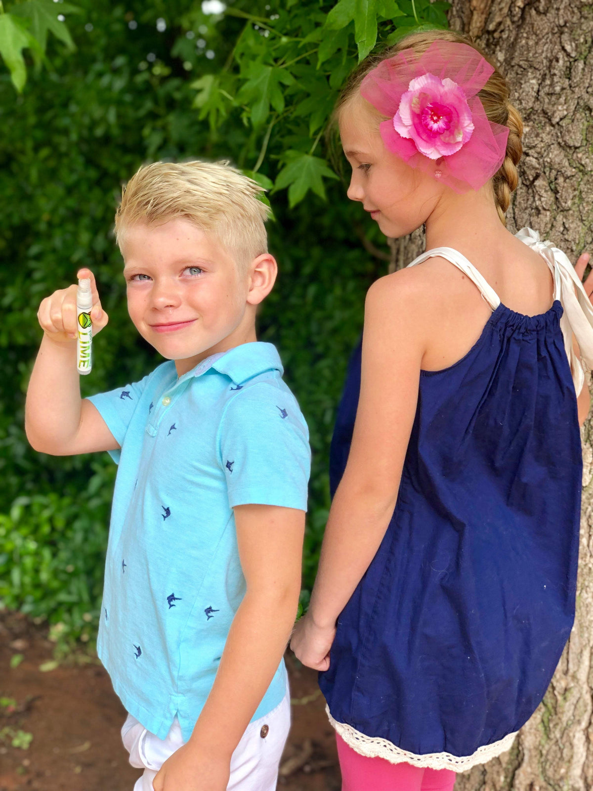 A young boy and girl stand next to each other outside. The young boy holds First Saturday insect repellent spray.